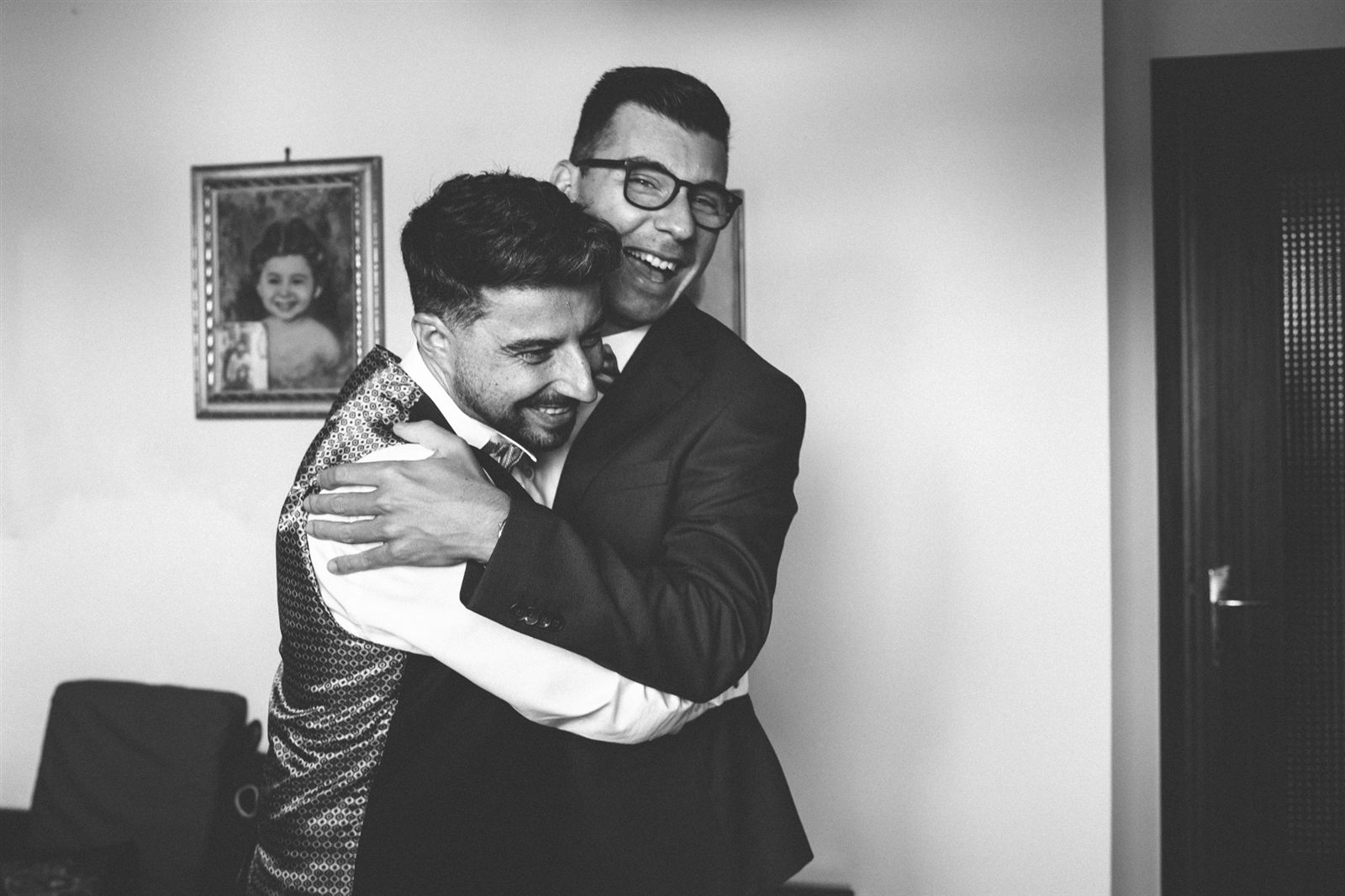 Lo sposo abbracciato al padre, con una vecchia foto sullo sfondo, bianco e nero Lo sposo abbracciato al padre, con una vecchia foto sullo sfondo, bianco e nero