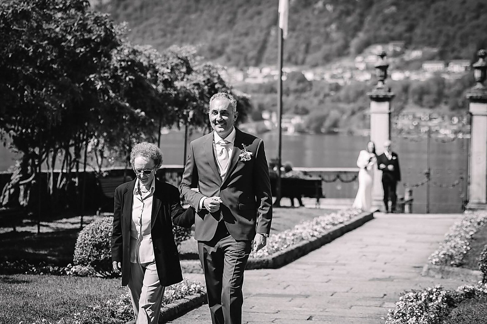 Lo sposo a braccetto con la madre lungo il vialetto, bianco e nero Lo sposo a braccetto con la madre lungo il vialetto, bianco e nero