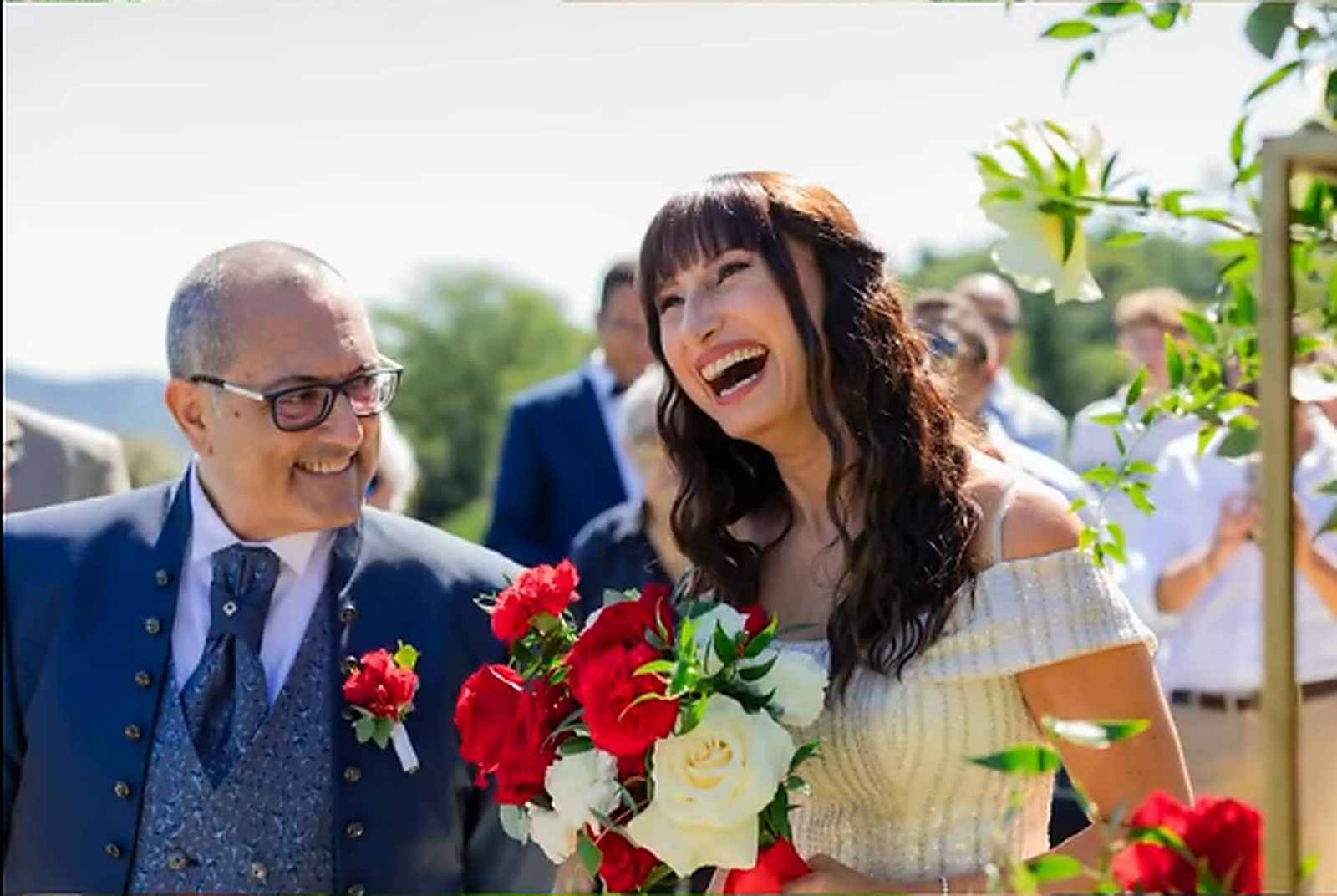 La sposa ride raggiungendo l'altare, il bouquet rosso fra le mani La sposa ride raggiungendo l'altare, il bouquet rosso fra le mani