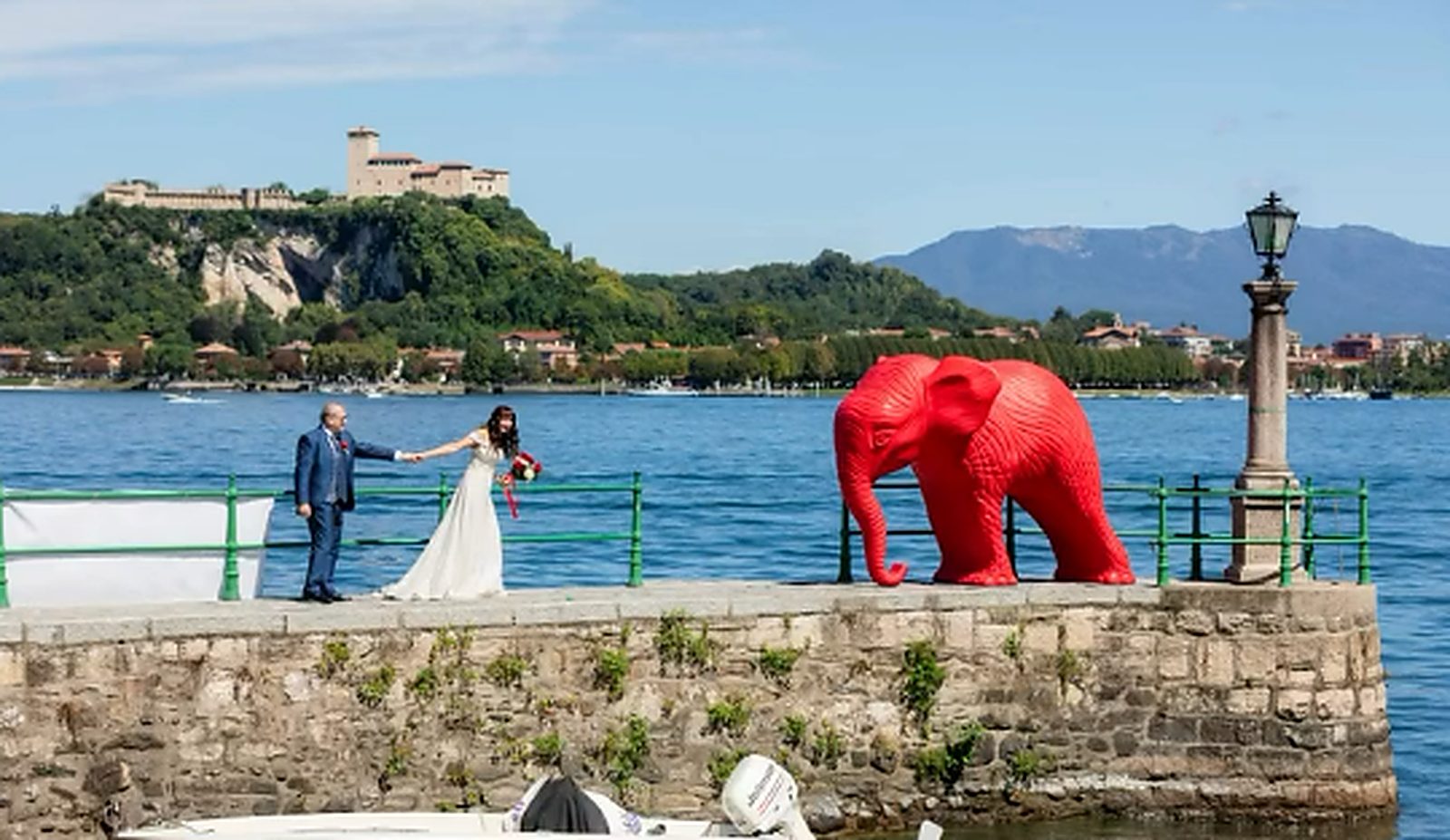Gli sposi mano nella mano sul molo, la Rocca di Angera sull'altra sponda