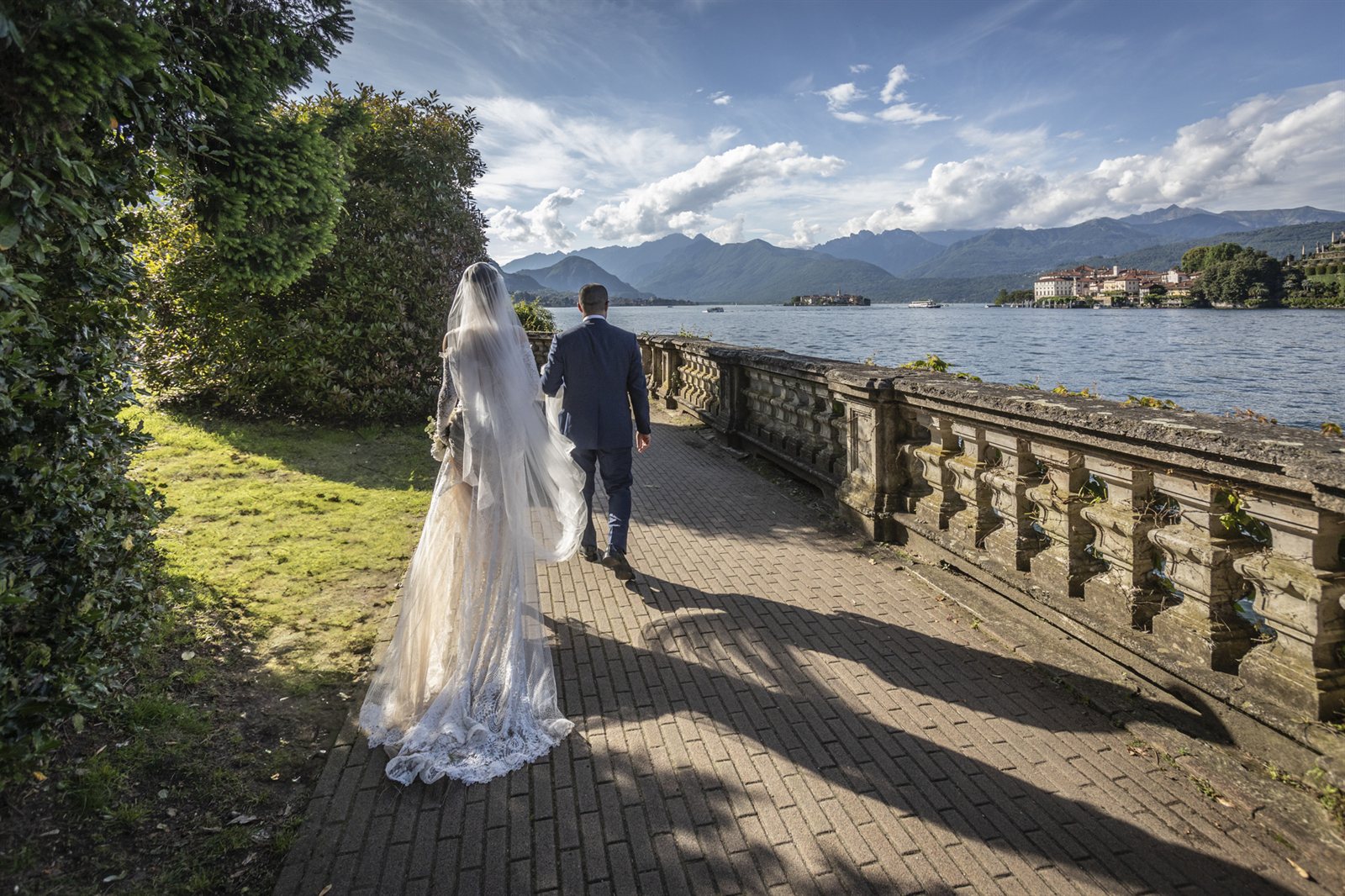 Gli sposi sulla passeggiata a lago di Villa Aminta, Stresa, con le montagne del Lago Maggiore