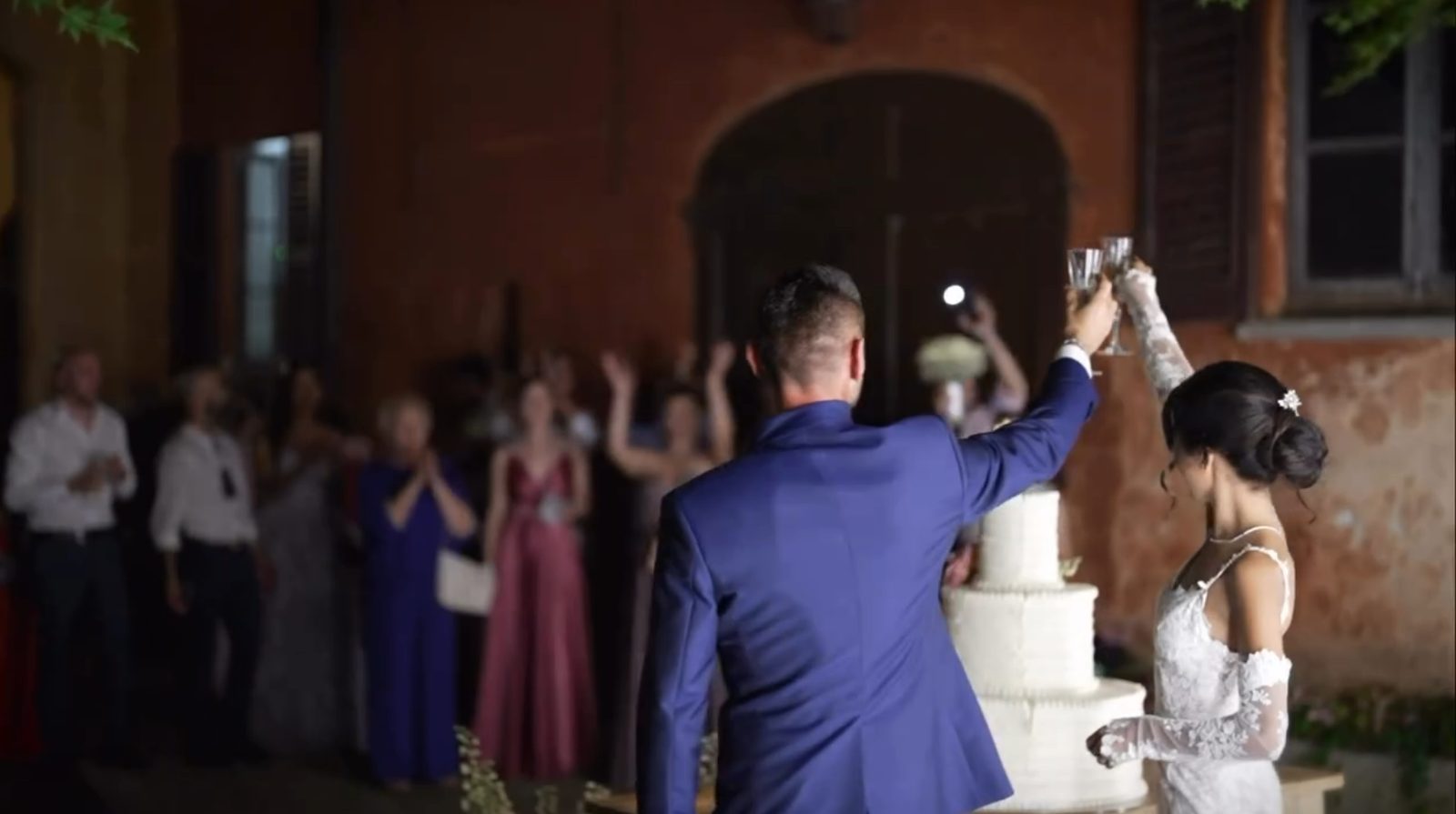 Il brindisi davanti alla torta, la villa illuminata di sera